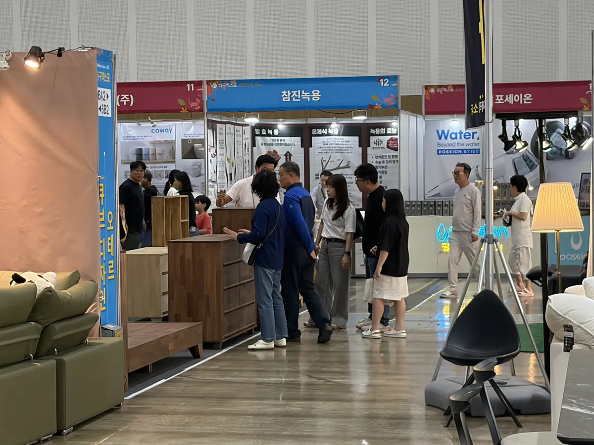 People browse wooden furniture displays at an indoor trade show