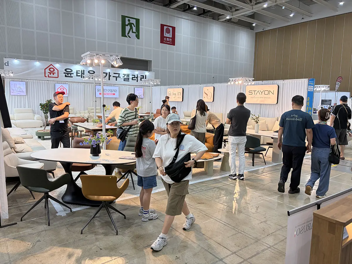 Busy furniture expo hall with sofas tables and chairs on display visitors browse booth displays under bright lighting