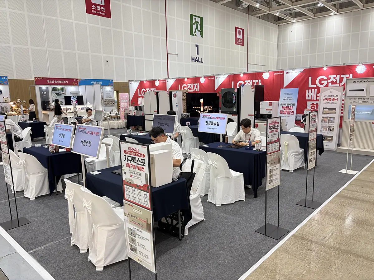 Exhibition hall showing an LG Electronics booth with red banners display stands and attendees seated at navy draped tables