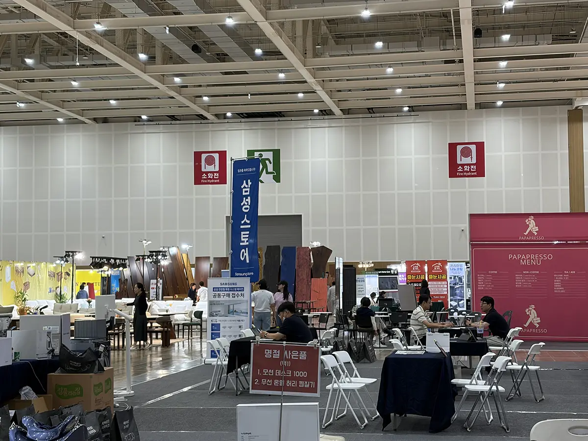 Indoor exhibition hall with multiple booths tables and chairs set up for a trade show signs in Korean and pink Papresso display in the background