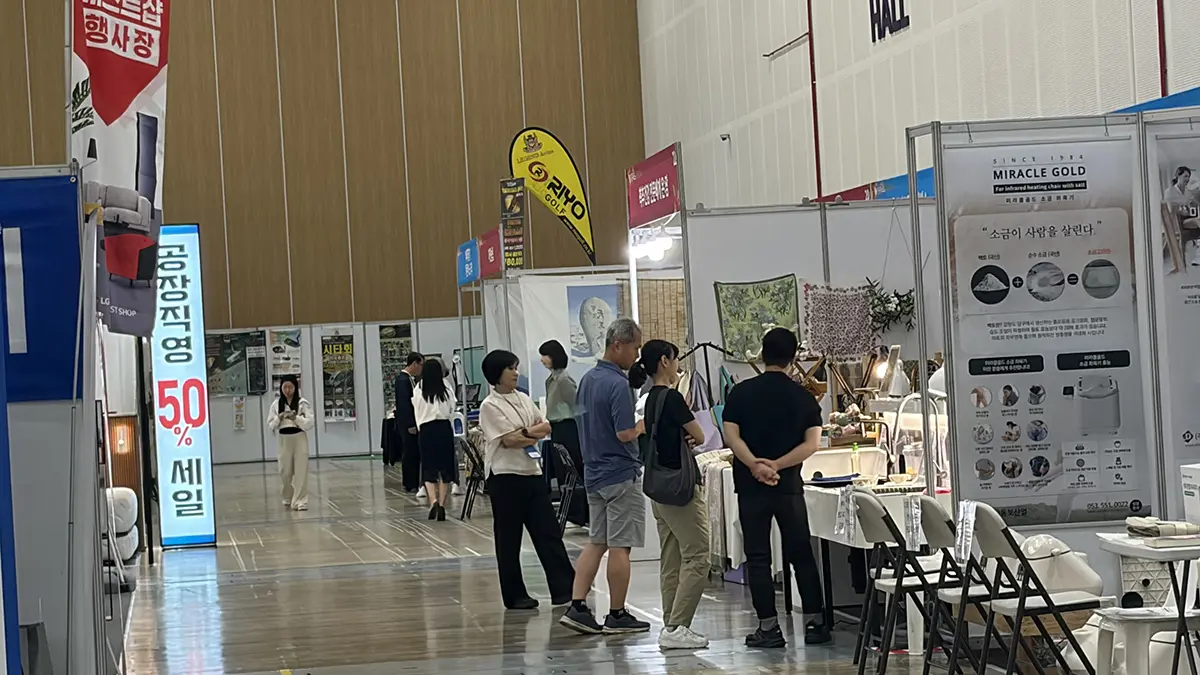 Indoor exhibition hall with multiple booths and attendees browsing displays a tall blue vertical sign shows 50 in Korean beside the walkway