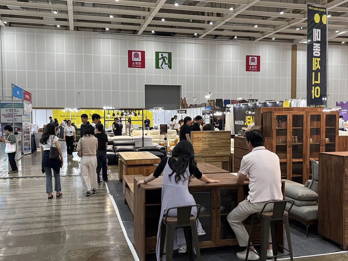 People browsing a furniture exhibition hall with wooden tables and cabinets on display in the foreground