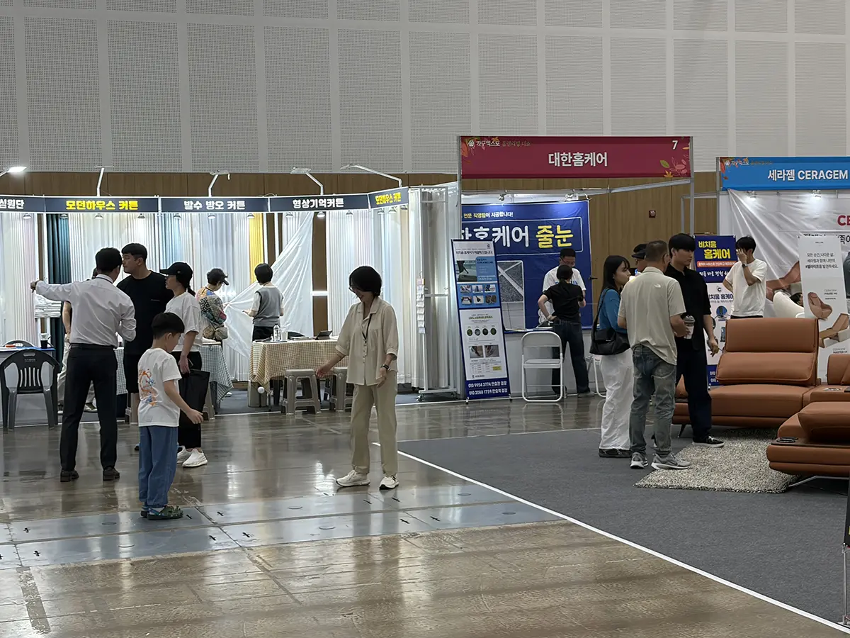 Exhibition hall with multiple vendor booths and people browsing a brown leather sofa display on the right side