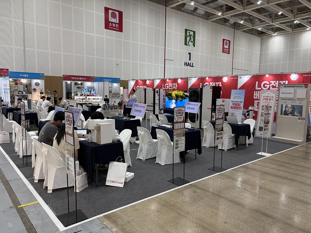 Trade show hall with red LG booth banners rows of tables with white chair covers and attendees working at the tables