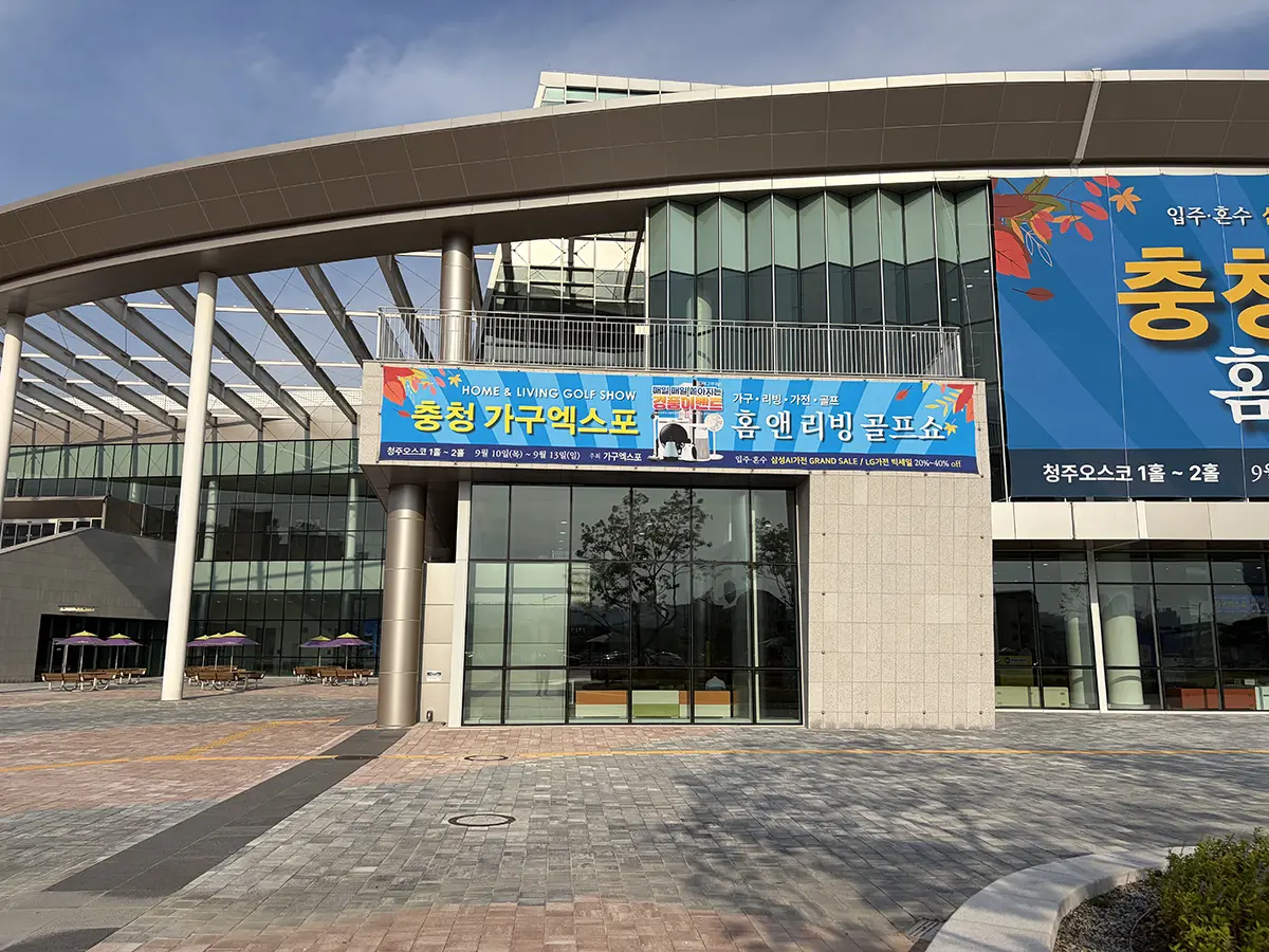 Modern building entrance with glass walls and a large blue banner advertising a home  living expo in Korean under a curved overhead structure